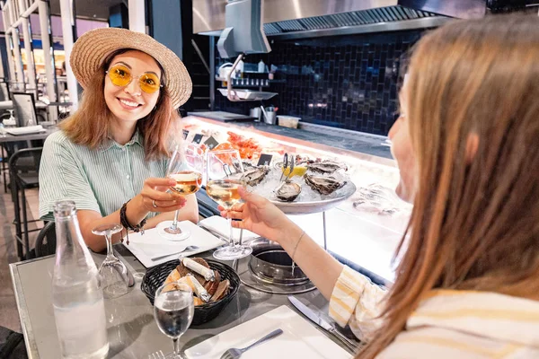 Two female friends in a restaurant eating oysters and shellfish and drinking white wine — Stock Photo, Image