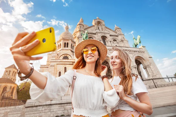 İki kız arkadaş Montmartre tepeüzerinde Sacre Coeur Bazilikası arka plan karşı selfie çekmek. Fransa'ya birlikte seyahat etmek