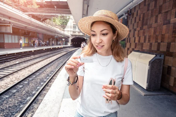 Портрет азіатської дівчини, що тримає невеликий електронний смарт-квиток і чекає на поїзд на залізничній платформі. Транспортний збір та концепція подорожей — стокове фото