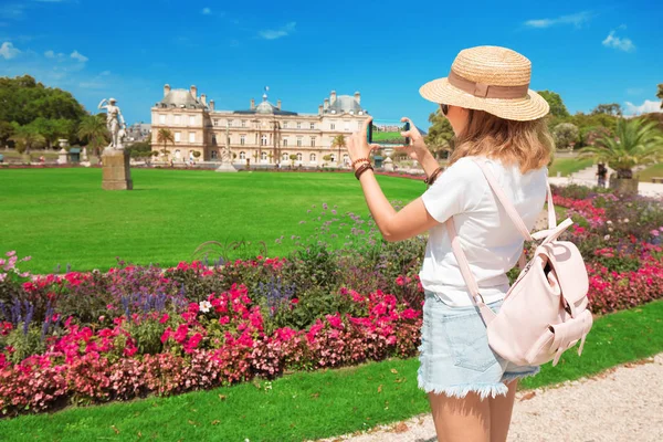 Nuori aasialaisen näköinen bloggaaja, joka ottaa kuvia älypuhelimella kaupunkimaiseman sosiaalisille verkostoille Luxemburgin puutarhassa Pariisissa. Vuosituhannen matkailu- ja elämäntapakonsepti — kuvapankkivalokuva