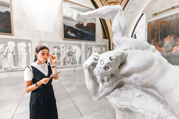 27 July 2019, Paris, France: Funny Asian art critic woman looks thoughtfully and puzzled at an ancient Greek statue in the Orsay Museum — Stock Photo, Image