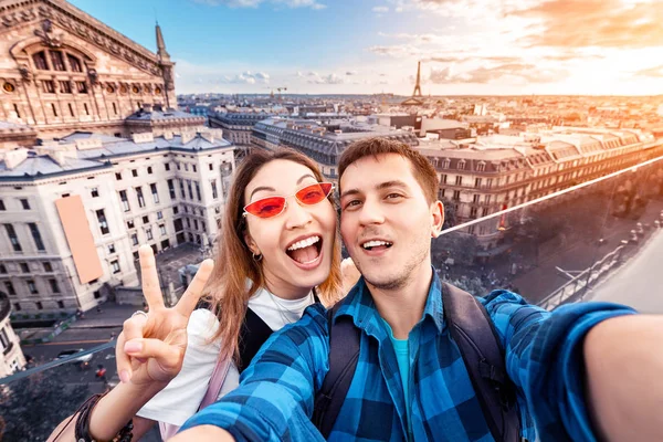Kärleksfullt par asiatisk tjej och europeisk kille kram och ta en selfie på observation däck med utsikt över parisiska landskapet. Smekmånad i Frankrike — Stockfoto