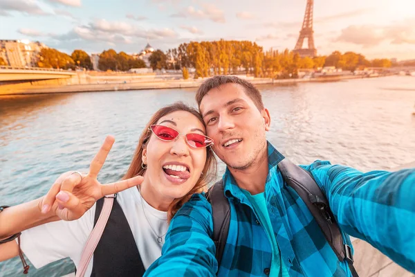 Aşık mutlu bir çift bir adam ve bir kadın kucaklamak ve arka planda Eyfel kulesi ile Seine nehri kıyısında bir selfie çekmek. Paris ve Fransa'da seyahat ve tatil