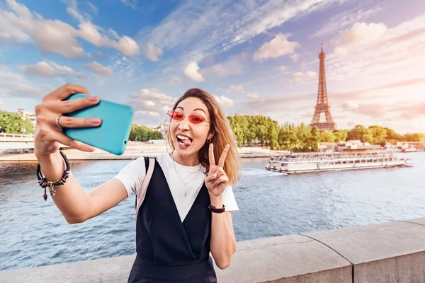 Chica asiática en un traje elegante y gafas de color rosa toma una foto selfie en el fondo de las principales atracciones de París la torre Eiffel a orillas del río Sena — Foto de Stock