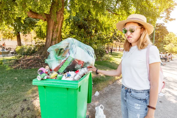 The annoyed girl throws the garbage into the already filled garbage container. The concept of environmental pollution and inaction of the authorities — Stock Photo, Image