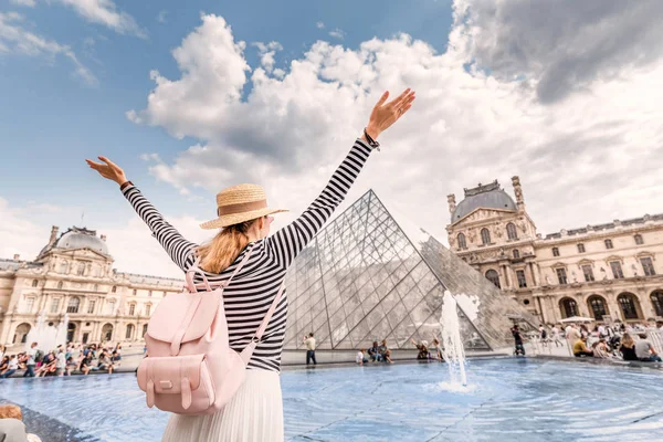 Uma menina feliz com uma mochila abre os braços e olha para a pirâmide do Louvre. Viagens e turismo em Paris e França — Fotografia de Stock