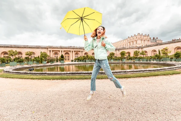 Feliz mulher asiática com guarda-chuva amarelo se divertindo no jardim real em Versalhes. Viajar em mau tempo conceito — Fotografia de Stock