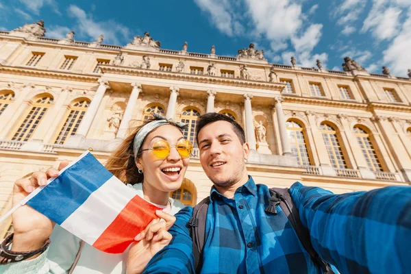 Um casal apaixonado, uma menina asiática e um homem europeu abraçam e tiram uma selfie contra o pano de fundo do Palácio Real de Versalhes, na França. Viagens e lua de mel — Fotografia de Stock