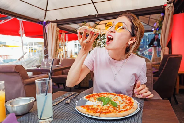 Mladá dívka jíst lahodnou pizzu se sýrem a zeleninou v pizzerii — Stock fotografie