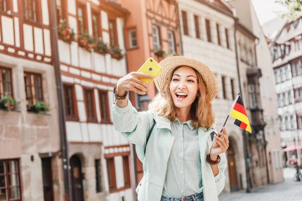 Young asian woman tourist taking selfie photo with german flag near the famous half-timbered street in Nuremberg old town — Stok fotoğraf