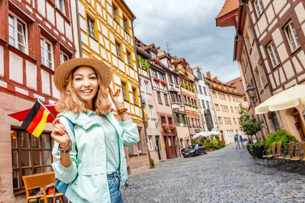 Νεαρή Ασιάτισσα τουρίστρια που ταξιδεύει με γερμανική σημαία κοντά στο διάσημο δρόμο με τα μισά ξύλα στην παλιά πόλη της Νυρεμβέργης — Φωτογραφία Αρχείου