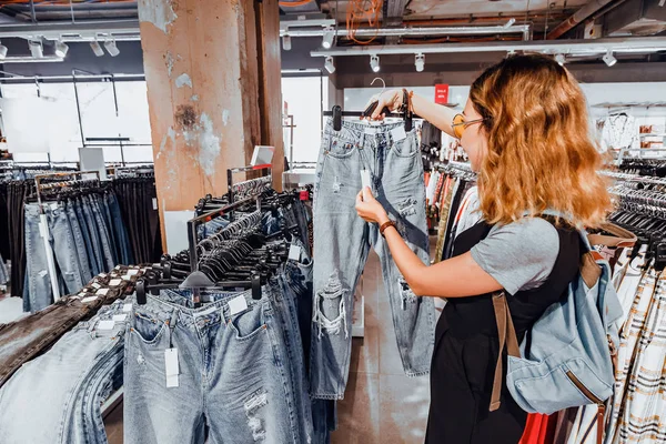 Mujer asiática feliz buscando jeans en tienda de ropa. Compras y concepto de estilo de vida — Foto de Stock