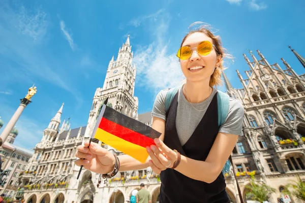 A happy girl with a German flag poses against the background of the city hall in Munich. Travel and immigration to Germany — Stock Photo, Image