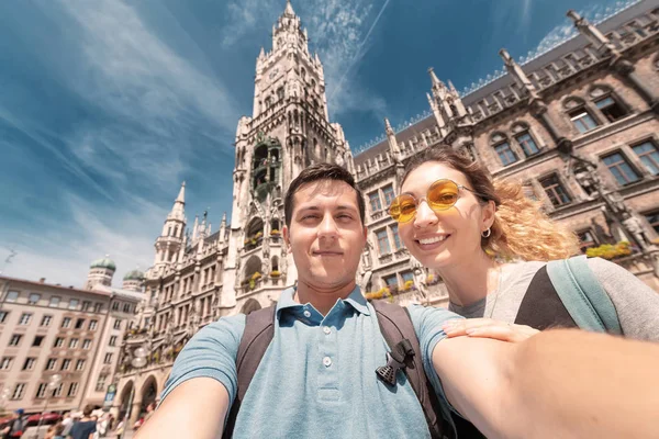 Feliz pareja multinacional en el amor abrazos y toma una foto selfie en el fondo de la torre del ayuntamiento en Munich. Viaje de luna de miel a Alemania —  Fotos de Stock