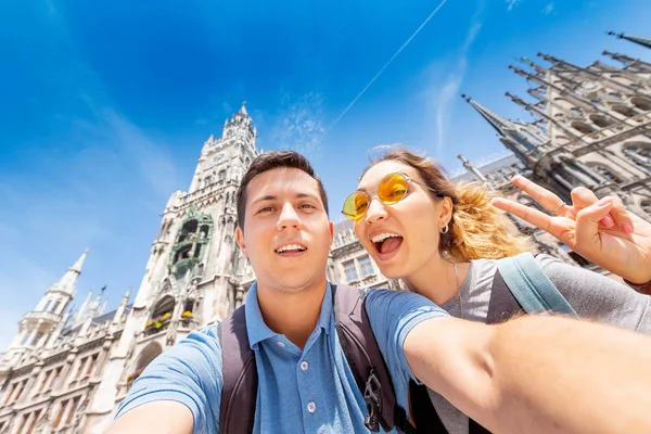 Glada multinationella par i kärlek kramar och tar en selfie foto på bakgrunden av stadshuset tornet i München. Bröllopsresa till Tyskland — Stockfoto