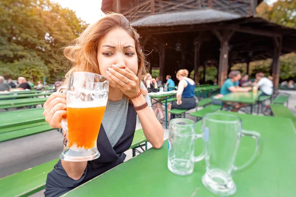 Девушка пробует пиво с выражением отвращения в уличном баре. Концепция алкогольного отравления и бросить пить — стоковое фото