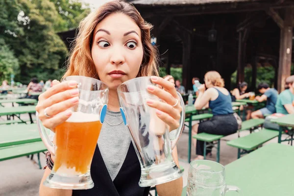 Смешная и сумасшедшая азиатка с двумя пивными на террасе пивного ресторана в Германии. Концепция похмелья и путешествия на фесте — стоковое фото
