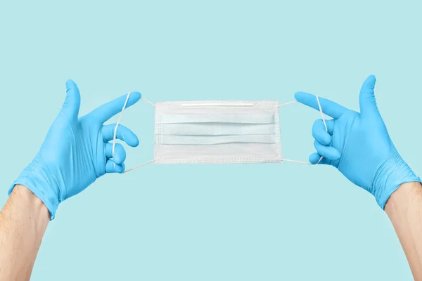 Medical face mask with hands in gloves, isolated on blue background. Coronavirus quarantine and contagion concept