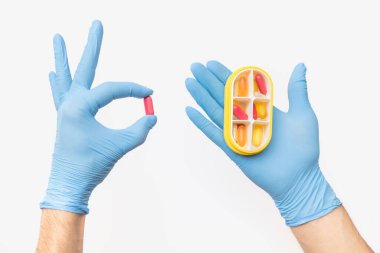 Tıbbi eldiven giyen doktor hasta için günlük dozda ilaç içeren bir tablet tutuyor. İlaç şirketleri kavramı ve hastalıkların tedavisinde yeni ilaçlar