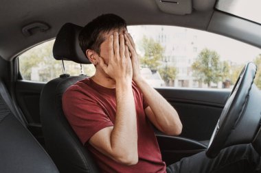 Genç adam arabasında otururken ellerini umutsuzca kapadı. Fazla çalışma ya da trafik kazası ve hata konsepti