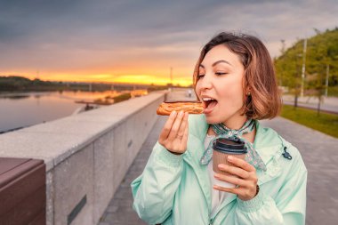 Asyalı mutlu kız taze Fransız tatlısını yer ve kahve içer. Sokak yemeği servisi. Şehir sehpasında eğlence ve eğlence.