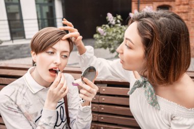 İki komik kız arkadaş aynaya bakarak kozmetik uyguluyor ve oynaşıyorlar..