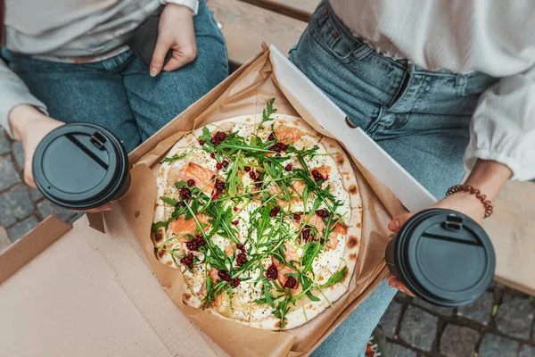 Girls friends have a break and eat delivered pizza and two mugs of coffee. Fast food Lunch on the street and communication concept