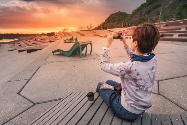 Дівчина Фотографує Красивий Захід Сонця Своєму Телефоні Сидячи Лавці Міському — стокове фото