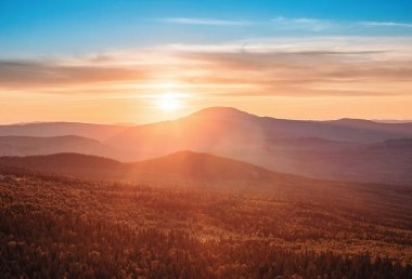 Vahşi ormanlarla kaplı kayalık bir dağ sırası batan güneşin altın ışığıyla aydınlatılıyor. Doğal park rezervi ya da av alanı. Eğlence amaçlı turizm.