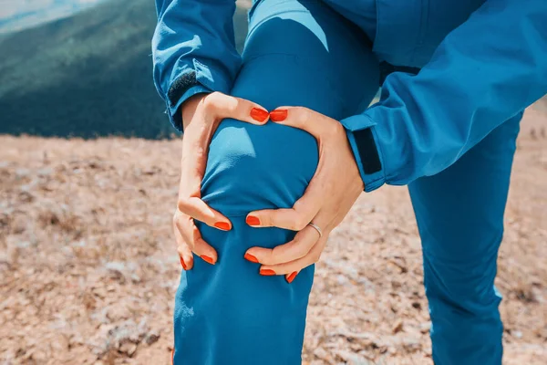 Woman is holding on to the knee joint, suffering from acute pain. Concept of injury of meniscus during a hike in the highlands