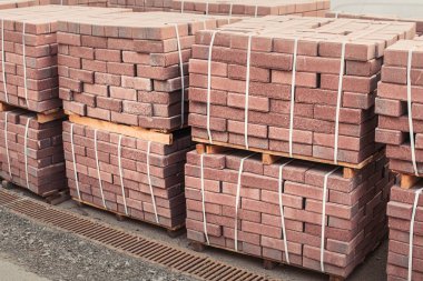 Sokaktaki bir inşaat deposunda yeni üretilen kırmızı tuğla paketleri. Onarım ve inşaat malzemeleri kavramı