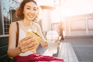 Mutlu kadın karnını doyurarak fast food yiyor ve bir iş gününden sonra sokakta oturup dinleniyor. Sağlıklı gıda ve ekstra kalori kavramı