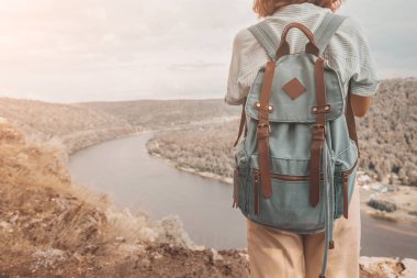 Sırt çantalı bir kadın uçurumun tepesinde durur ve bir nehrin ya da gölün manzarasına hayran kalır.