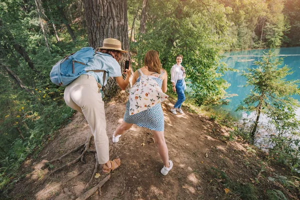 Kadın arkadaşlar blogları ve sosyal medyaları için komik pozlar vererek parktaki bir gölün yakınında fotoğraf çekiliyorlar. Akıllı telefonlara ve genç neslin kameralarına bağımlılık