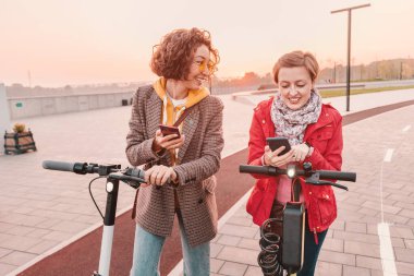İki bayan arkadaş elektrikli scooter kiralamak ve kiralamak için akıllı telefonlarındaki uygulamayı kullanıyor. Şehir sokaklarında modern ulaşım