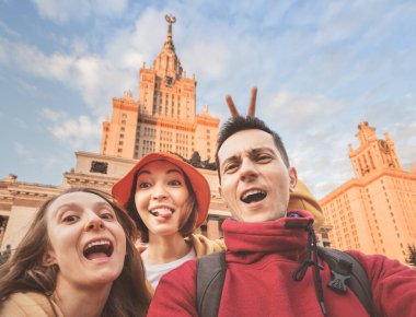 Üç arkadaş öğrenci Moskova Eyalet Üniversitesi 'nin ana kampüsünün arka planında selfie çekiyorlar. Okul yılının başlangıcı veya gezi konsepti