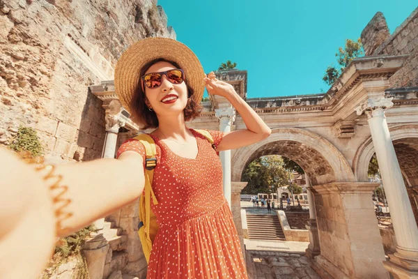 Happy female tourist traveller takes selfie photos against the backdrop of Hadrian\'s gate - a popular attraction in the old city of Antalya, Turkey