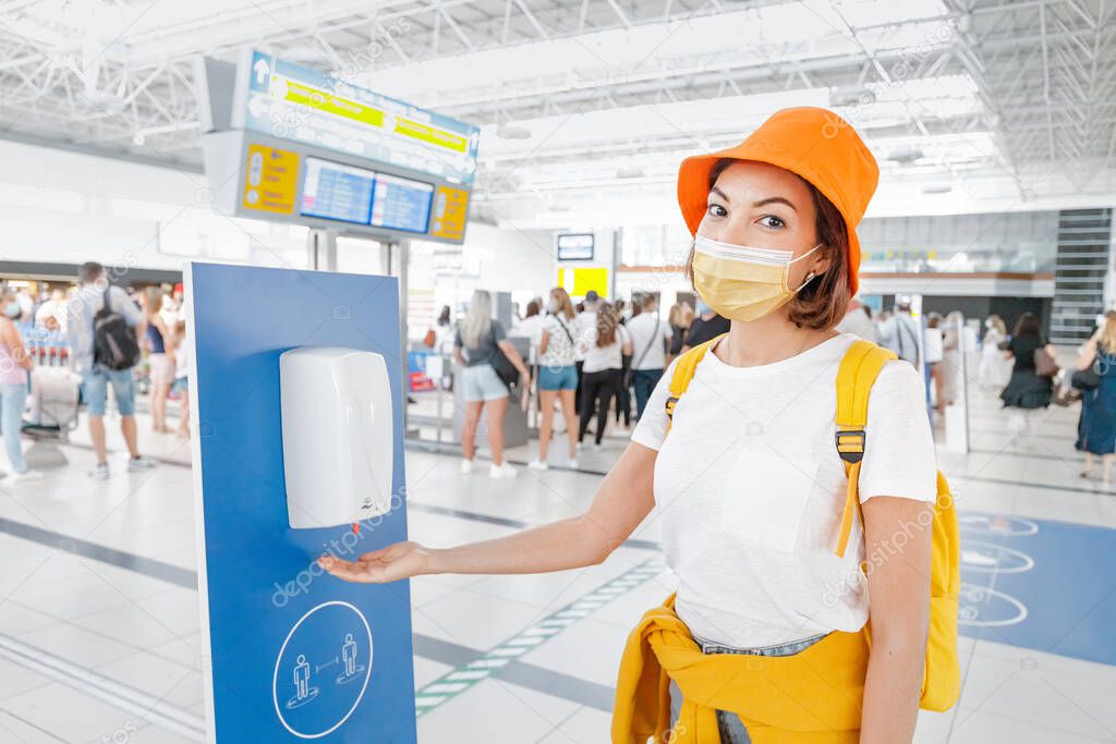 A female passenger disinfects her hands with an automatic sanitizer dispenser in the airport. Health care and protection from infection during the coronavirus pandemic