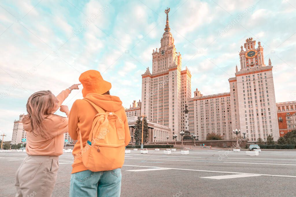Female friends travel to tourist attractions in Moscow. One woman student tells and shows the other details of the architecture of the Moscow University building.