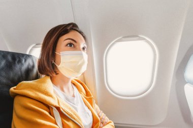 Asyalı bir kız uçak uçuşu sırasında tıbbi maske takıyor. Hava taşımacılığı yolcuları için güvenlik kavramı ve yeni davranış kuralları