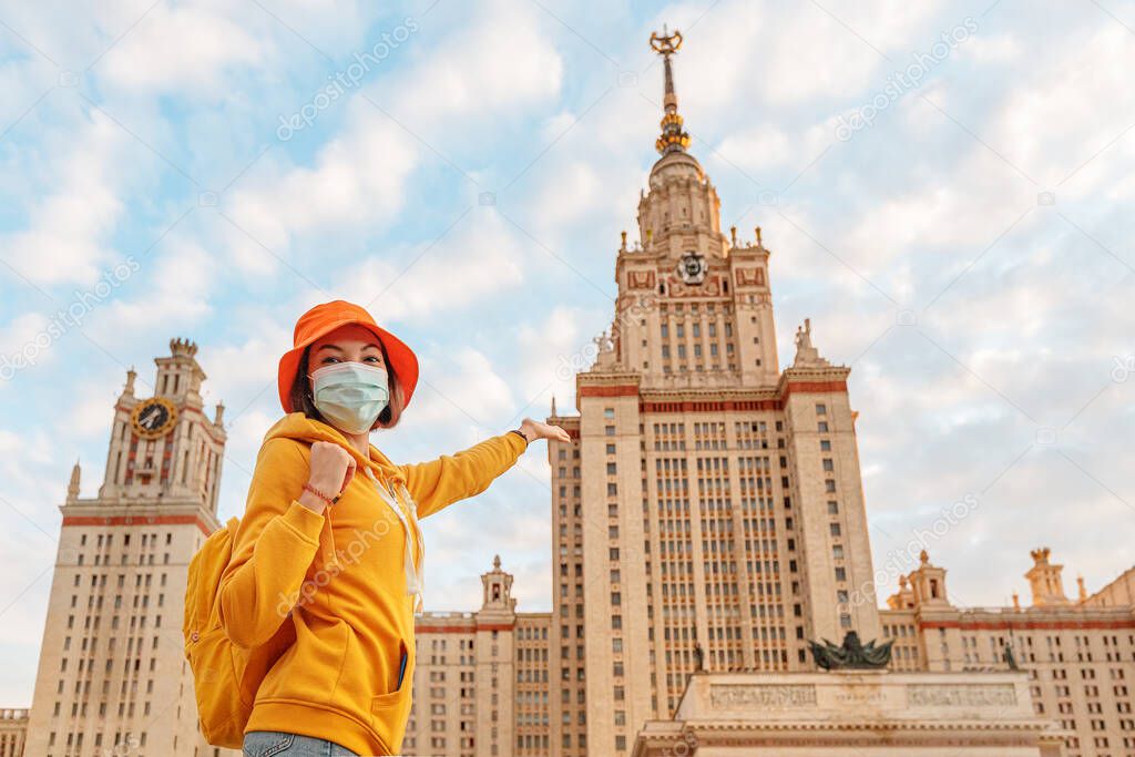 Happy female young student wearing medical mask rejoices of the beginning of the school year in front of the main building of Lomonosov Moscow State University.