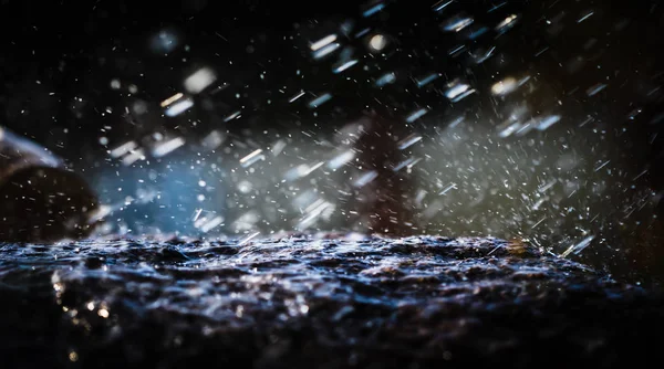 Wet stone in the rain. Rain water drop falling to the stone. Water is flowing and splashing around them.