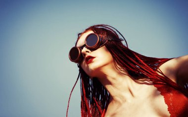 Kızıl saçlı göz kamaştırıcı bir kız, kırmızı bir mayo ve mavi gökyüzü arka planında kaynakçı pozları. Metnin için boş yer