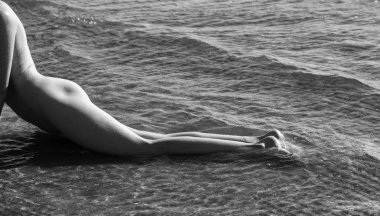 Doğanın tadını çıkaran güzel bir kız. Genç çıplak kadın sahilde denizin tadını çıkarıyor. Arkadan bak.