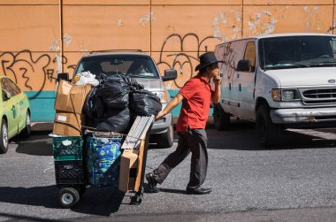 New York, Amerika Birleşik Devletleri - 23 Eylül 2017: Manhattan sokak sahne. Paketleri tam sepeti ile New York City caddeden aşağı yürüyüş teslimatçı. Genç adam bir şapka ve kırmızı gömlek bir sepeti eşyalarını ile çeker.