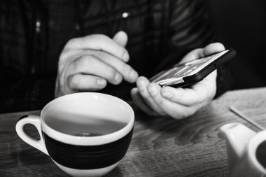 Bir adam bir kafede çay, bir smartphone yazarken ve okurken içme dinleniyor. Mobil ofisinde çalışıyorum. Yakın çekim yumuşak odak alan sığ derinliği görüntüsüyle. Siyah beyaz resim