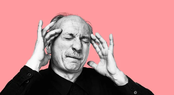 Old man feeling tired and headache. Strong headache. Health care concept. Black and white image of an old man suffering from a headache isolated on coral pink background