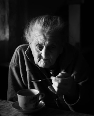 Yaşlı bir depresif kadın siyah beyaz görüntü. Yaşlı bir yalnız kadın mutfağa yakın pencere ve çay içme bir masada oturur.