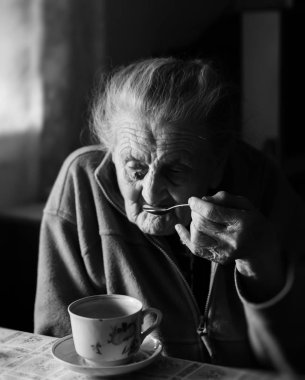 Yaşlı bir depresif kadın siyah beyaz görüntü. Yaşlı bir yalnız kadın mutfağa yakın pencere ve çay içme bir masada oturur.