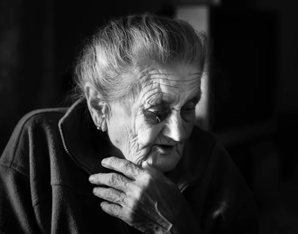 一个沮丧的老太婆的黑白形象 一位孤独的老年妇女坐在窗户附近厨房的一张桌子旁喝茶 — 图库照片